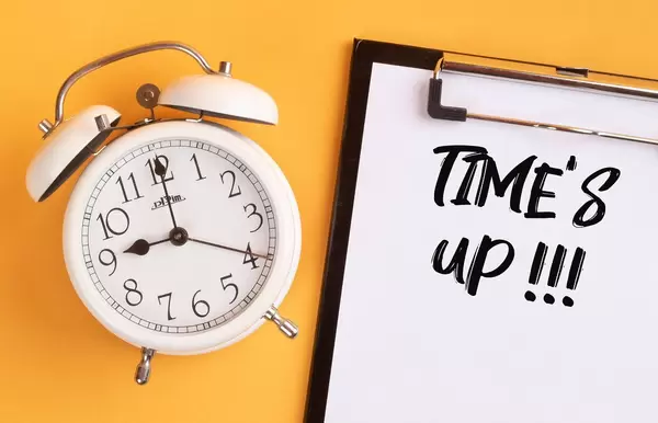 Alarm clock with handwritten text Time's Up on clipboard