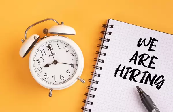 Alarm clock with handwritten text We Are Hiring on yellow background