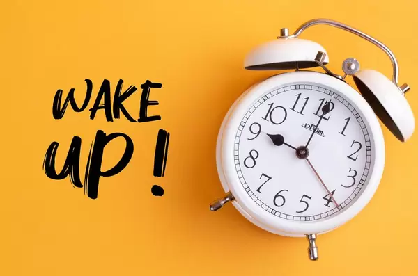 Alarm clock with handwritten Wake Up text on yellow background