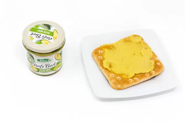 Allos - aufs Brot Bio Avocado-Creme im Glas und auf einem Cracker auf weißem Teller