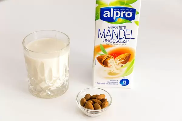 Almond milk by Belgium manufacturer Alpro, unsweetened, next to a glass of vegan milk and a small bowl with whole nuts