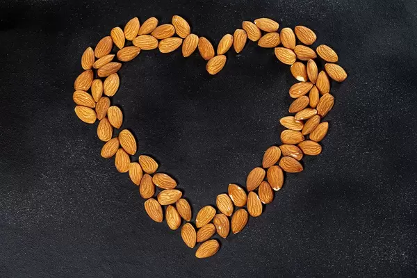 Almond nuts on a black background lined in the shape of a heart. Top view (Flip 2019)