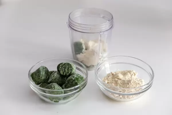 Almond protein powder and frozen spinach in glass bowls and mixer vessel, as ingredients for a high-energy smoothie