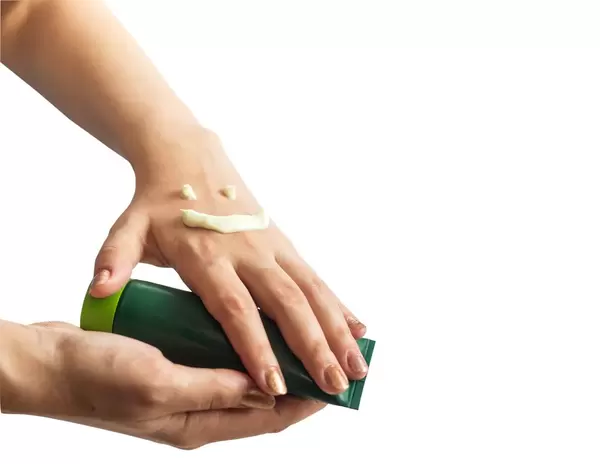 Als lachendes Gesicht aufgetragene Handcreme auf Frauenhänden, die Tube halten