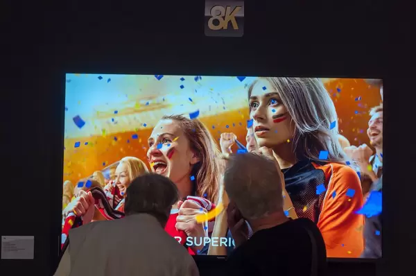 Ältere Messebesucher schauen sich einen 8K Fernseher aus der Nähe an