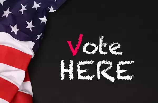 American flag with the text Vote Here against a blackboard background