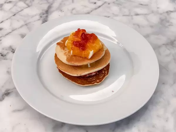 American Pancakes gestapelt mit einer Scheibe Orange und Roter Konfitüre auf einem weißen Teller