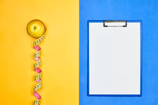 An apple with measuring tape and blank A4 paper