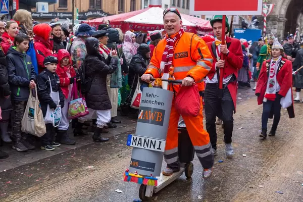 An employee of the Cologne waste management company AWB rides a wooden scooter with a bin and collects some rubbish at the Rose Monday Parade in Cologne