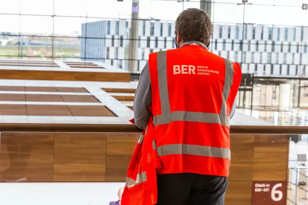An employee wearing an orange safety vest with the logo of the BER Berlin Brandenburg Airport