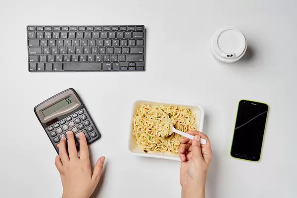 An office worker eating instant noodles at workspace and working