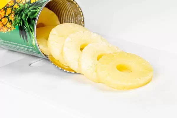 Ananas Scheiben aus der Dose vor weißem Hintergrund mit weißem Schneidebrett