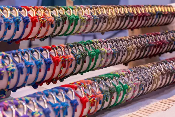 Aneinandergereihte farbenfrohe Armbänder für Bootfans aus Tauen und Ösen auf rundem Holz