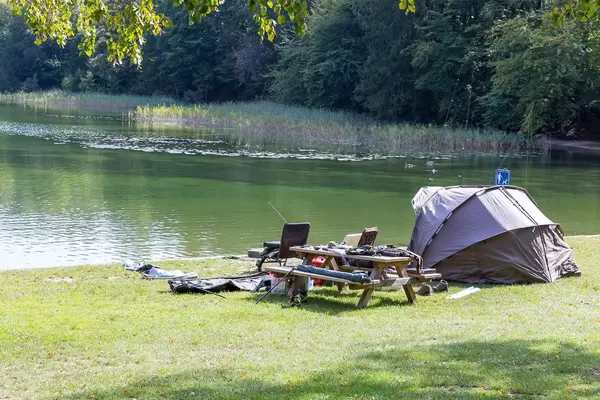 Angeln am Reintalersee: Zelt und Campingstühle neben Holzbänken und Tisch mit Angelausrüstung