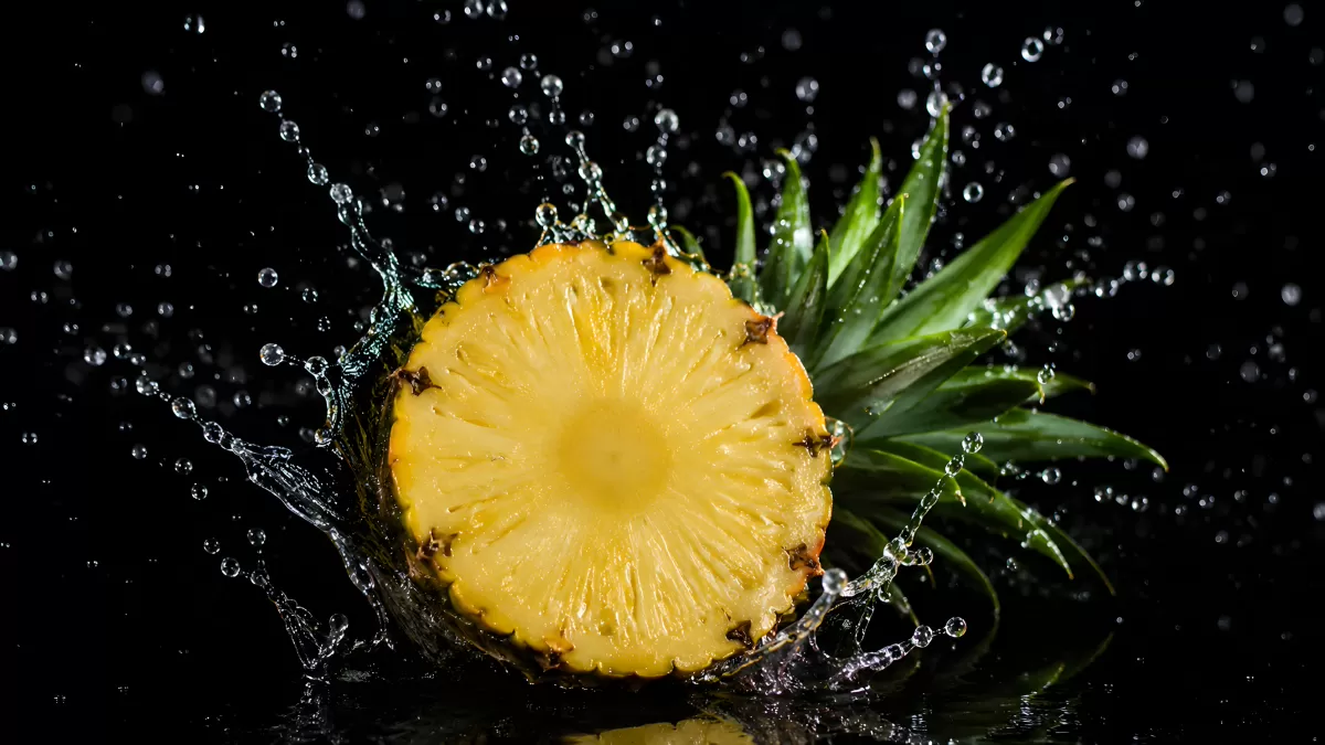 Angeschnittene Ananas mit Wasserspritzern vor schwarzem Hintergrund
