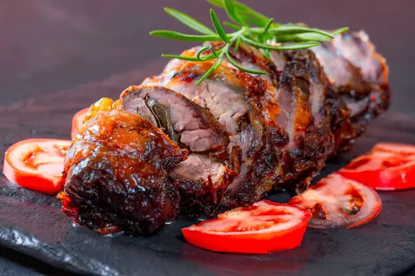 Angeschnittener Hackbraten verziert mit Rosmarin und Tomatenscheiben auf schwarzem Hintergrund