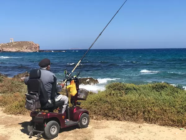Angler auf Griechenland: Alter Mann sitzt mit seiner Angel im Elektromobil an der Küste der Insel Naxos