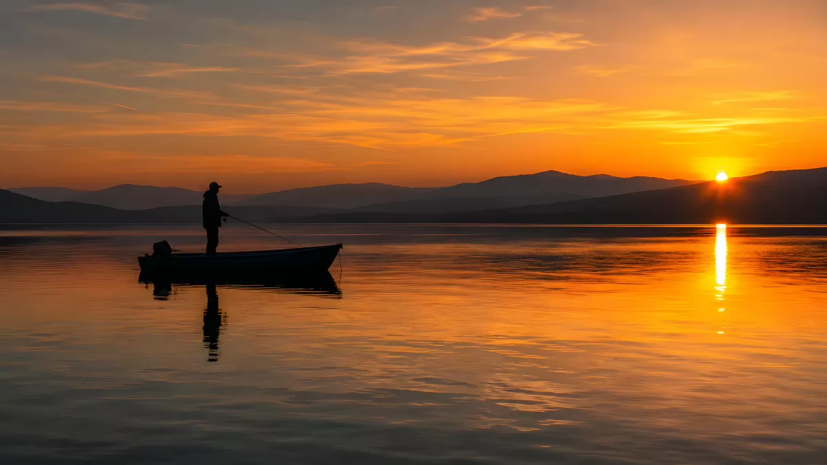 Angler im Boot bei goldenem Sonnenuntergang am See