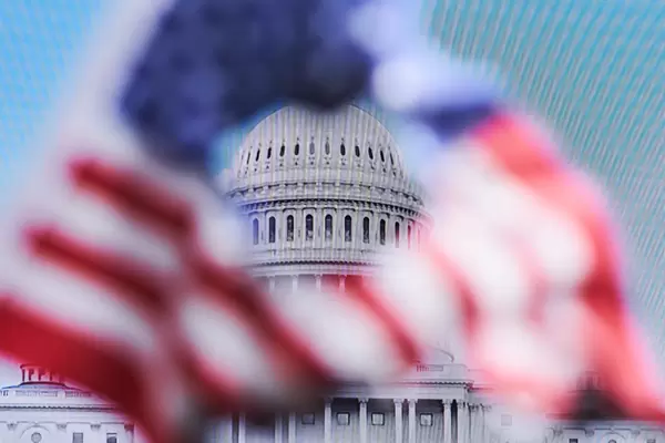 Angriff auf US-Kapitol: USA-Flagge mit Loch in der Mitte vor Fernseher, der das Kapitol zeigt