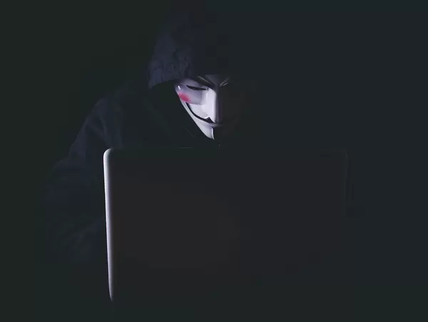 Anonymous man in mask and hoodie sitting near laptop
