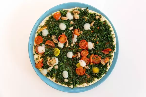 Ansicht von oben auf die Fleischersatz-Pizza Verdura der Trattoria Alfredo, in vier Stücke geteilt und mit veganem Belege wie Spinat, Pilzen und Tomaten