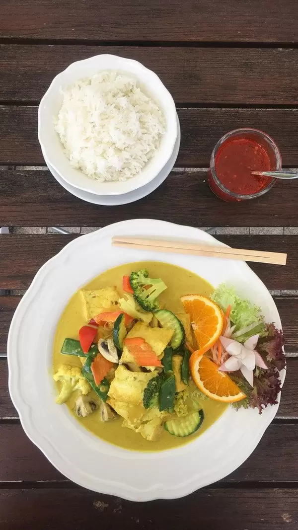 Ansicht von oben auf ein asiatisches, fleischloses Gericht mit ausgewogenem Gemüse und Orange in einer veganen Curry-Kurkuma Sauce, neben Reis