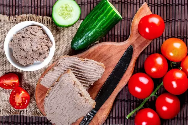 Ansicht von oben, auf ein geschmiertes Brot mit Leberwurst auf einem Frühstücksbrettchen, neben frischem Gemüse