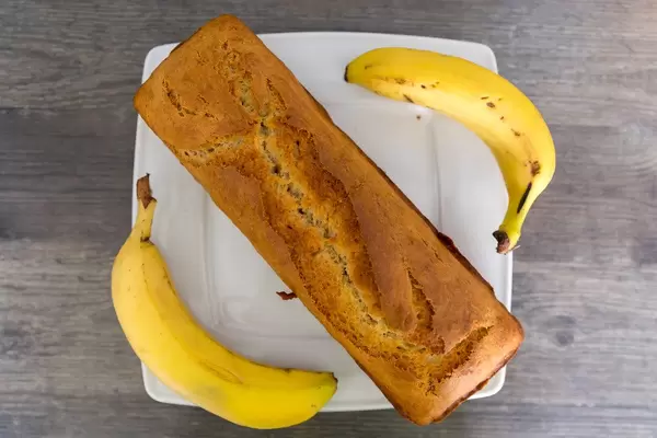 Ansicht von oben auf ein kastenförmiges Bananenbrot neben zwei ganzen Bananen