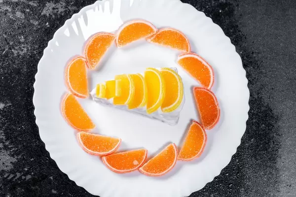 Ansicht von oben auf einen Limonenkuchen mit gezuckerten Orangenscheiben, auf einer schwarzen Arbeitsfläche