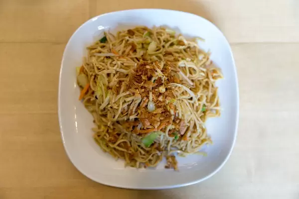 Ansicht von oben auf gebratene Nudeln mit buntem Gemüse und Ei, auf einem weißen Teller auf einem Holztisch, als vegetarische Hauptspeise
