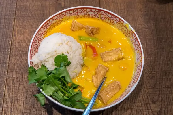 Ansicht von oben auf gelbes veganes Tofu-Cocos-Curry, Paprika, Champignons, Süßkartoffeln, Babyspinat, Blumenkohl, Bohnen und Jasmin-Duftreis