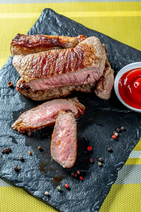 Ansicht von oben auf geschnittenes Steak mit Tomatensoße und Pfefferkörnern auf Schieferplatte