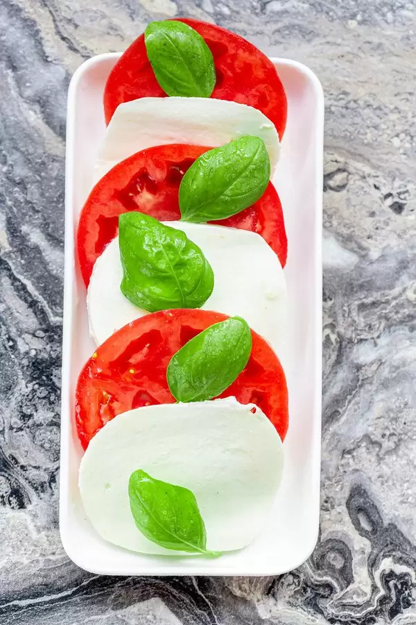 Ansicht von oben auf italienischen Mozzarella, großen Tomatenscheiben und einzelnen Basilikumblättern