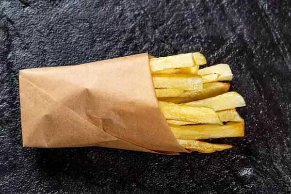 Ansicht von oben auf knackige Pommes Frites in umweltschonender Papiertüte, auf schwarzem Untergrund