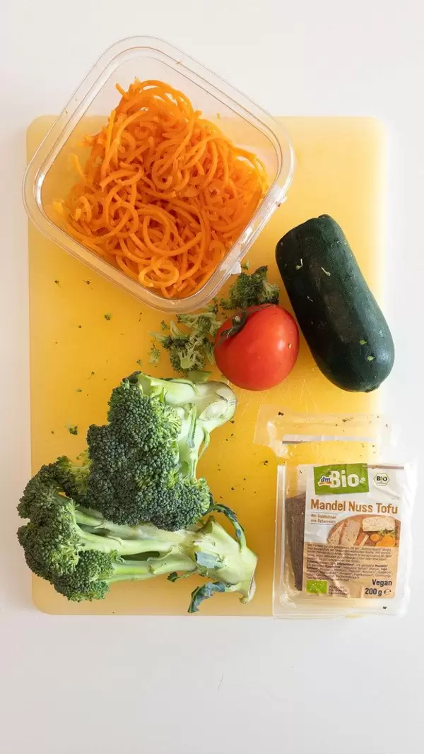 Ansicht von oben auf vegan Zutaten für ein ausgewogenes Mittagessen, mit Brokkoli, Tomate, Zucchini, Möhrenspaghetti und Mandel-Nuss-Tofu
