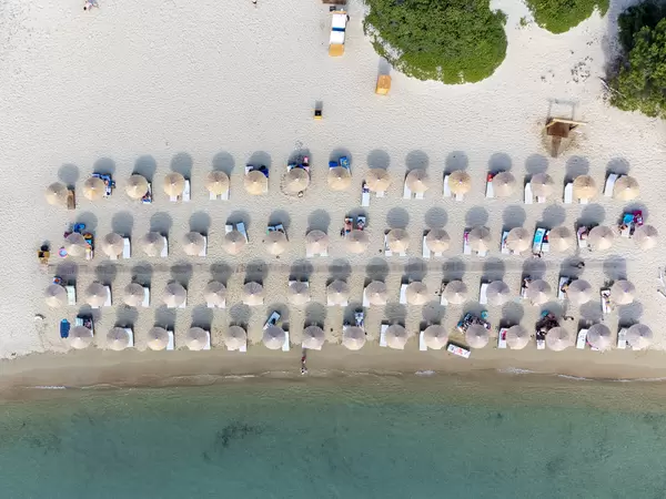 Ansicht von oben: vier Reihen Sonnenschirme am Sandstrand mit türkisem Wasser auf Tsoungria