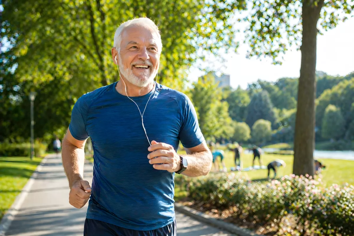 Anti Aging: Älterer Mann joggt lächelnd im sonnigen Stadtpark