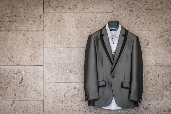 Anzug des Bräutigams in grau und schwarz mit weißem Hemd hängt auf Kleiderbügel an Wand