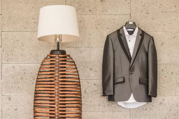 Anzug des Bräutigams mit weißem Hemd hängt auf Bügel an Wand neben moderner Lampe