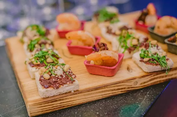Aperitif-Häppchen mit Shrimps, Toast, Fleischpaste und Nüssen auf Holzbrett