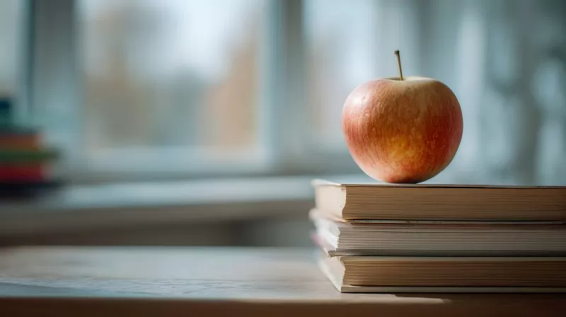 Apfel auf Bücherstapel vor Fenster im Klassenzimmer