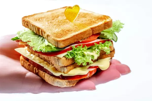 Appetitanregendes Sandwich mit Kopfsalattomatenkäse und -schinken auf der Hand des Mannes
