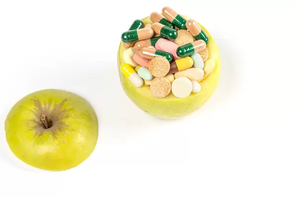 Apple filled with multi-colored medical pills and capsules on a white background
