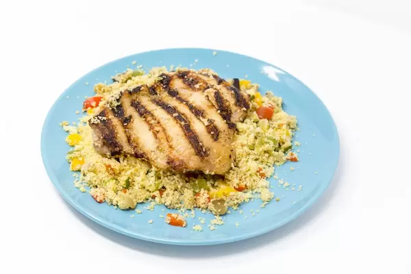 Arabisch gegrilltes Hähnchen auf Gemüsecouscous mit Razel Hanout Dip auf blauem Teller