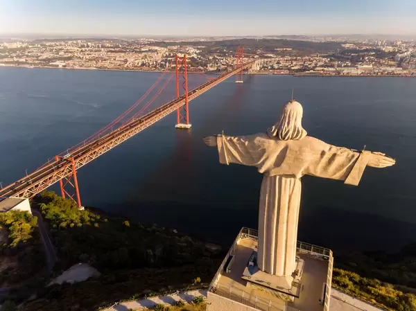 Areal view / drone shot from behind of Cristo Rei monument with Ponte 25 de Abril bridge in Almada Lisbon
