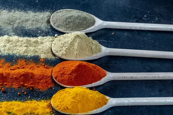 Aromatische Gewürze wie Kurkuma, Pfeffer und Ingwer auf Holzlöffel und auf dunklem Tisch