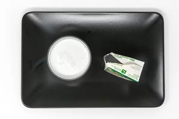 Aroy D - Coconut Milk in glas with packaging on black plate - Top View