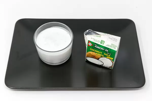 Aroy D - Kokosnussmilch im glas mit Verpackung auf schwarzem Teller