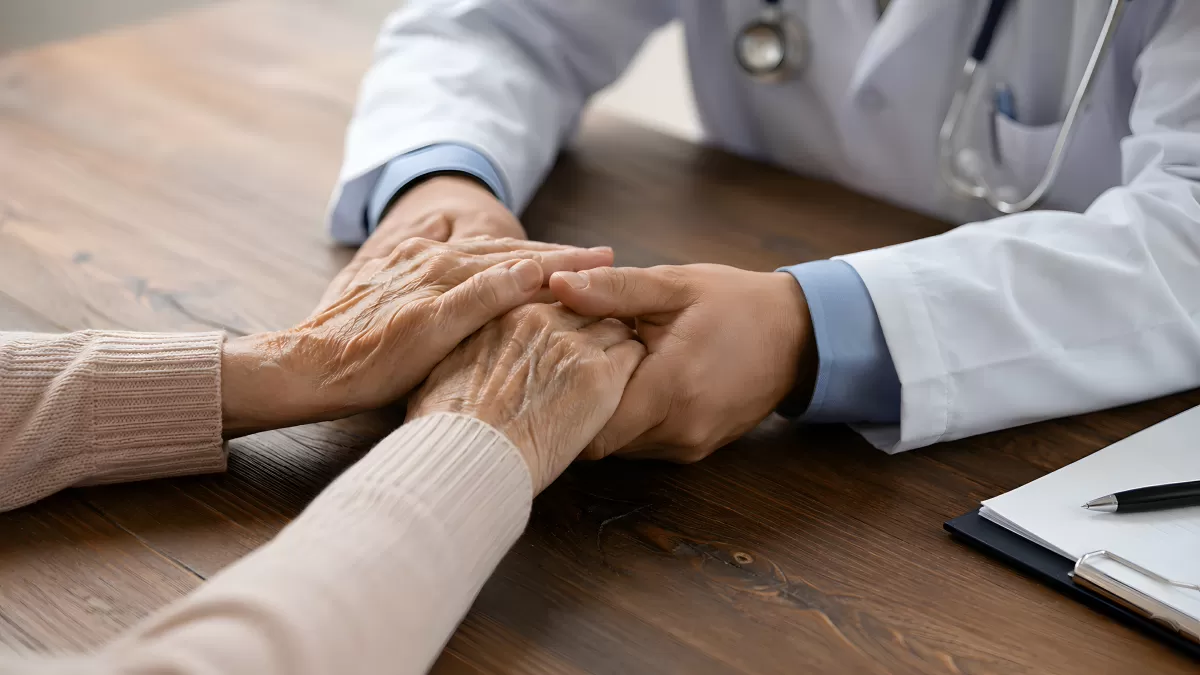 Arzt hält einfühlsam die Hände einer älteren Patientin
