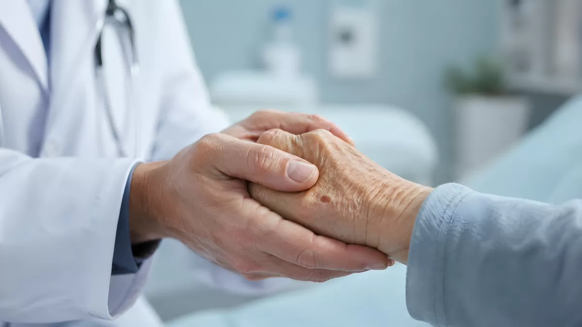 Arzt hält fürsorglich die Hand eines älteren Patienten